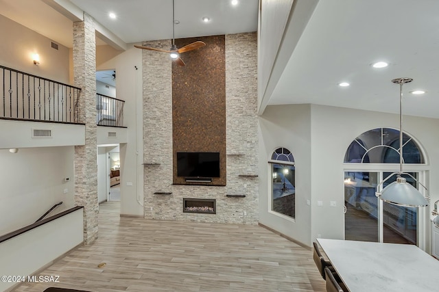 living room with a fireplace, a towering ceiling, light hardwood / wood-style flooring, and ceiling fan