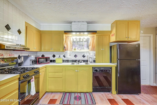 kitchen featuring a sink, black appliances, under cabinet range hood, light wood finished floors, and light countertops