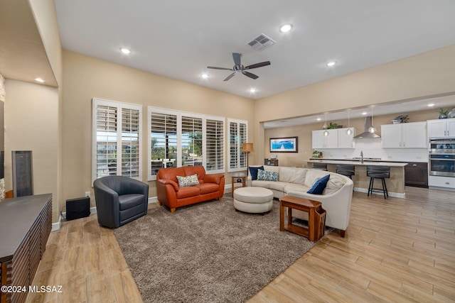 living room with ceiling fan, light hardwood / wood-style floors, and sink