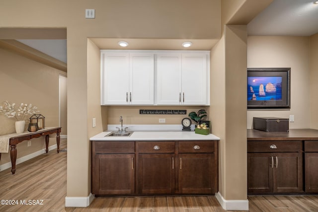 bar featuring dark brown cabinetry, sink, white cabinetry, and light wood-type flooring