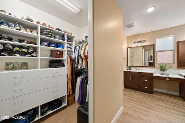 spacious closet with sink, built in desk, and light hardwood / wood-style flooring