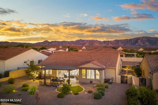 back house at dusk featuring a mountain view and a patio