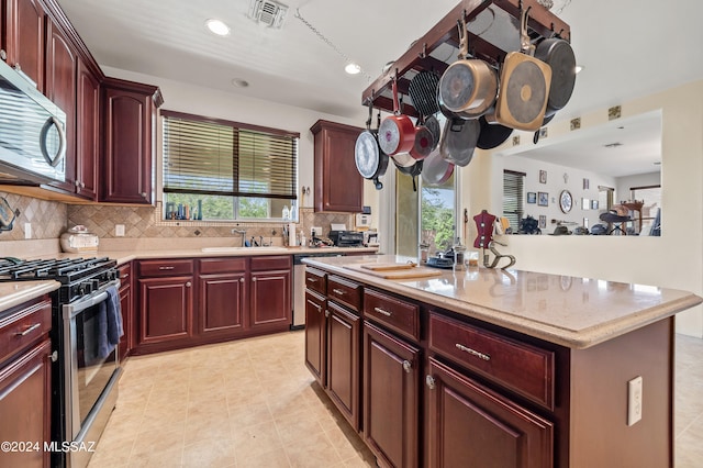 kitchen with sink, a center island, appliances with stainless steel finishes, light stone countertops, and backsplash