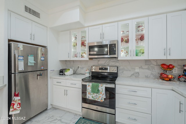 kitchen with decorative backsplash, white cabinets, light stone counters, and stainless steel appliances