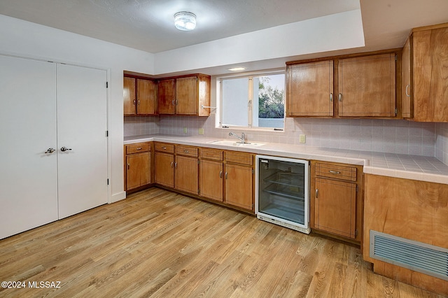 kitchen featuring wine cooler, sink, tasteful backsplash, and light wood-type flooring