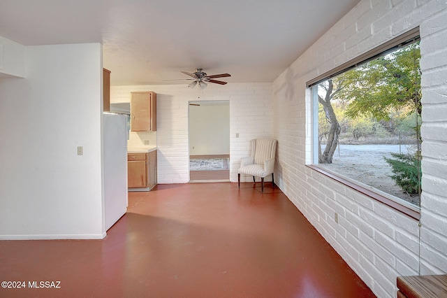 unfurnished room featuring concrete flooring, ceiling fan, and brick wall