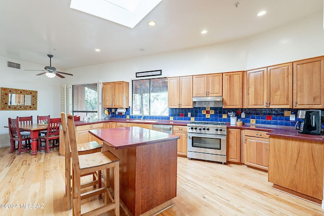 kitchen featuring appliances with stainless steel finishes, a skylight, a kitchen breakfast bar, a center island, and ceiling fan