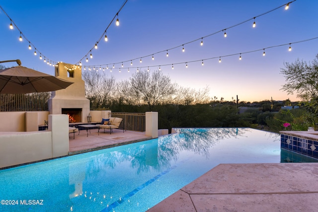 pool at dusk featuring a patio and an outdoor fireplace