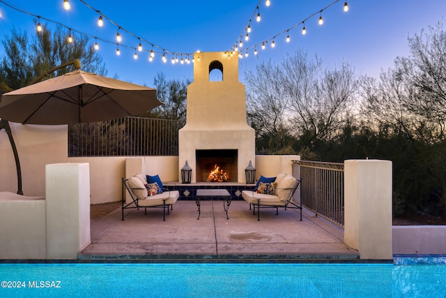 pool at dusk featuring a patio area and an outdoor fireplace