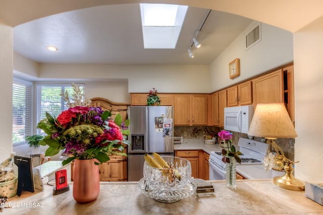 kitchen featuring rail lighting, tasteful backsplash, white appliances, kitchen peninsula, and a skylight