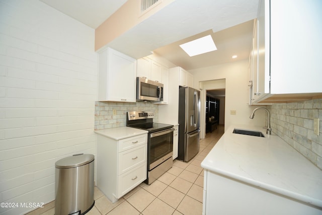 kitchen featuring tasteful backsplash, appliances with stainless steel finishes, white cabinetry, a skylight, and sink