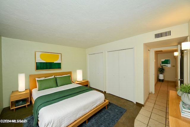 bedroom with dark tile patterned floors and two closets