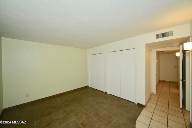 unfurnished bedroom featuring two closets and dark tile patterned flooring