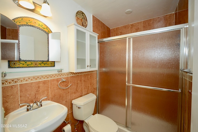 bathroom with a shower with door, tile walls, sink, and toilet