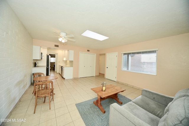 living room featuring light tile patterned flooring, brick wall, a skylight, and ceiling fan