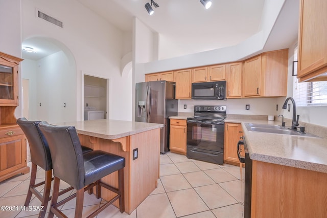 kitchen with black appliances, washer / clothes dryer, sink, a kitchen breakfast bar, and light tile patterned floors