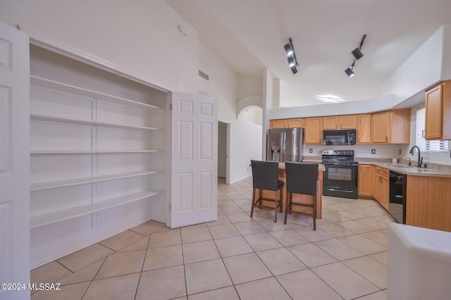 kitchen featuring black appliances, track lighting, a kitchen bar, sink, and light tile patterned flooring