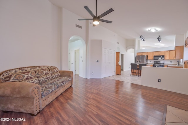 living room with ceiling fan, light hardwood / wood-style floors, high vaulted ceiling, and sink