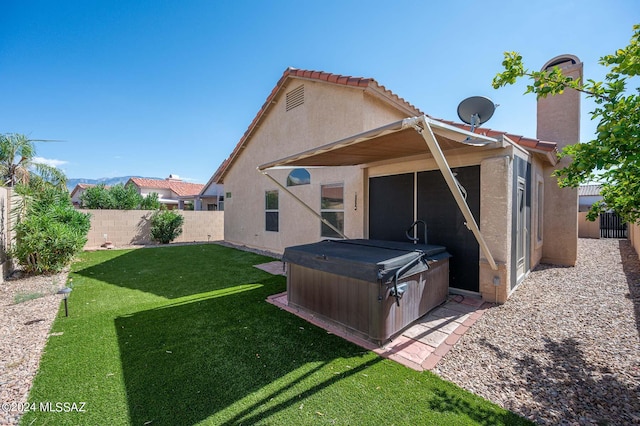 rear view of house with a hot tub and a yard