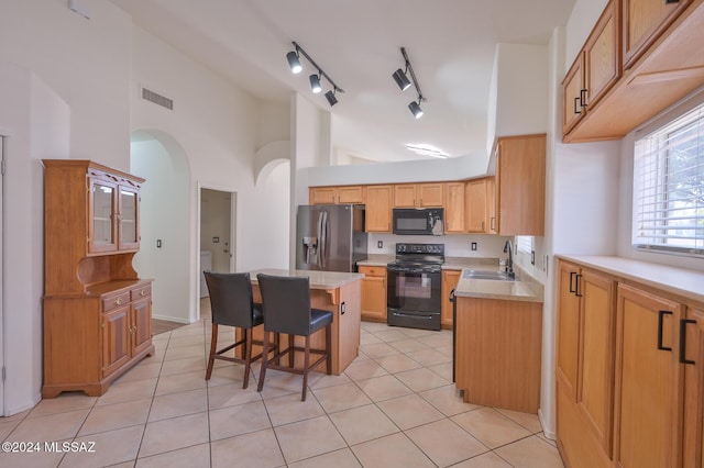 kitchen featuring a center island, black appliances, light tile patterned flooring, sink, and a breakfast bar area