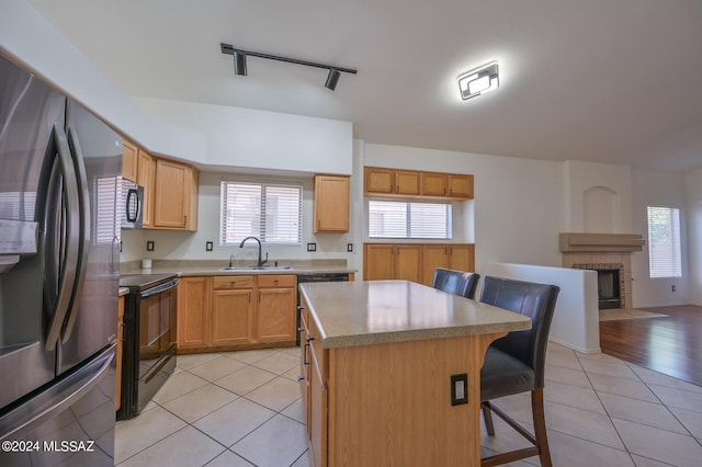 kitchen with a kitchen breakfast bar, light tile patterned flooring, a kitchen island, black appliances, and sink