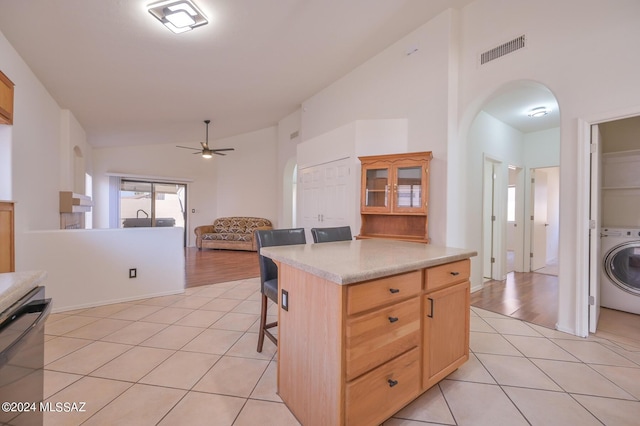 kitchen with lofted ceiling, washer / clothes dryer, light brown cabinets, black dishwasher, and a breakfast bar