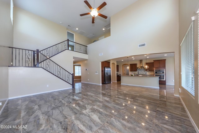 unfurnished living room with a towering ceiling, a ceiling fan, stairs, visible vents, and marble finish floor