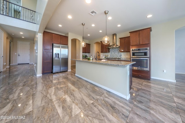 kitchen featuring wall chimney range hood, stainless steel appliances, arched walkways, marble finish floor, and a sink