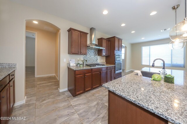 kitchen featuring wall chimney range hood, arched walkways, stainless steel appliances, and a sink
