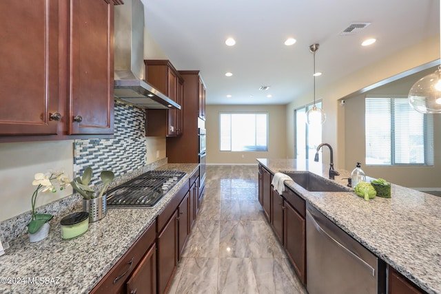kitchen with light stone counters, wall chimney range hood, visible vents, appliances with stainless steel finishes, and a sink