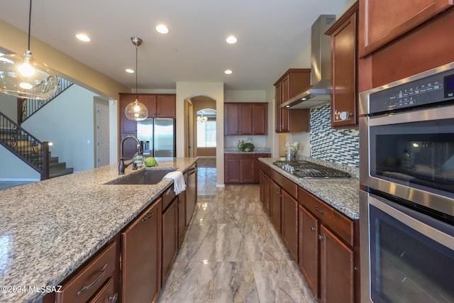 kitchen featuring arched walkways, wall chimney exhaust hood, stainless steel appliances, marble finish floor, and light stone counters