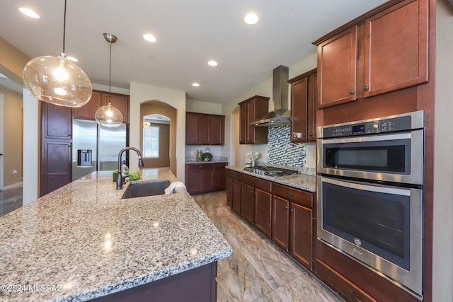 kitchen featuring arched walkways, wall chimney exhaust hood, a sink, appliances with stainless steel finishes, and recessed lighting