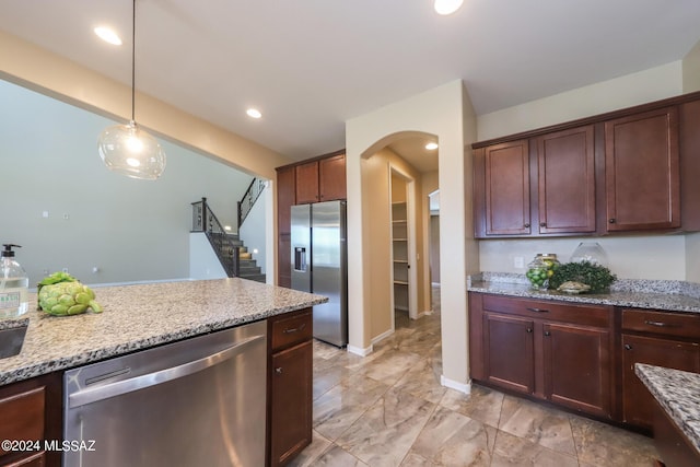 kitchen featuring arched walkways, appliances with stainless steel finishes, light stone counters, decorative light fixtures, and baseboards