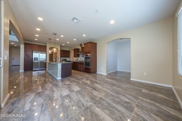 kitchen featuring wall chimney range hood, open floor plan, visible vents, appliances with stainless steel finishes, and arched walkways