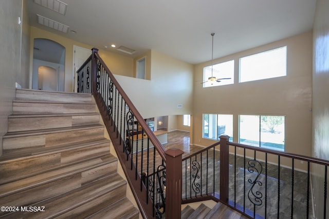 staircase featuring visible vents, a wealth of natural light, a ceiling fan, and wood finished floors