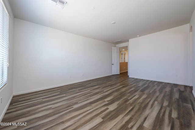 unfurnished room featuring visible vents, dark wood-style flooring, and baseboards