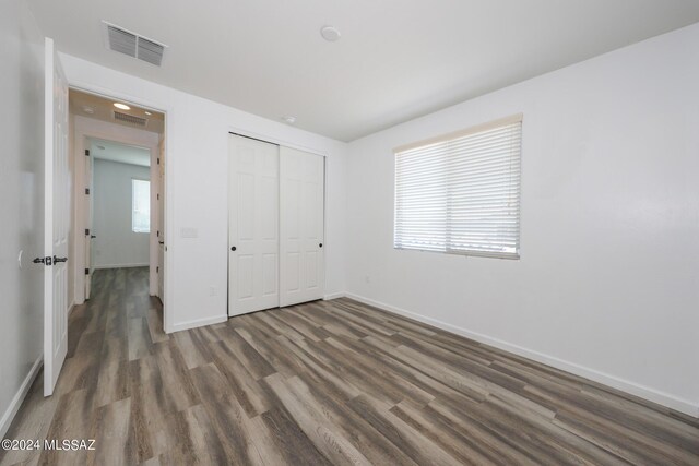 unfurnished bedroom featuring a closet, visible vents, baseboards, and wood finished floors