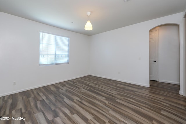 spare room featuring arched walkways, baseboards, and dark wood finished floors
