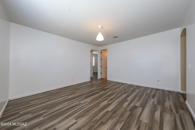 empty room with arched walkways, dark wood-style flooring, baseboards, and visible vents