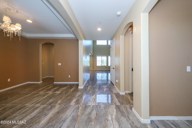hall featuring arched walkways, baseboards, and an inviting chandelier