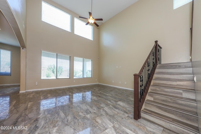 unfurnished living room featuring baseboards, high vaulted ceiling, stairs, and a ceiling fan