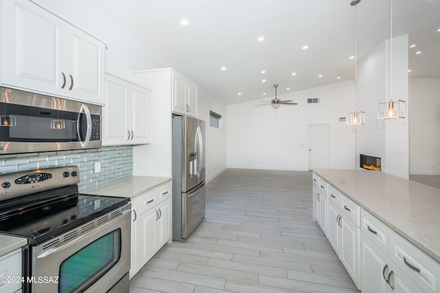 kitchen with decorative backsplash, stainless steel appliances, hanging light fixtures, white cabinets, and lofted ceiling