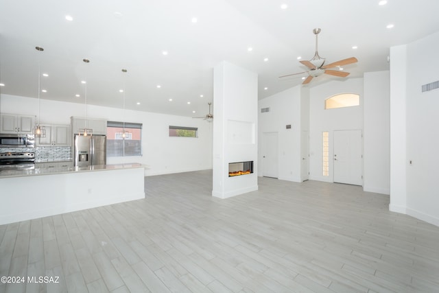 unfurnished living room with ceiling fan, light hardwood / wood-style floors, and high vaulted ceiling