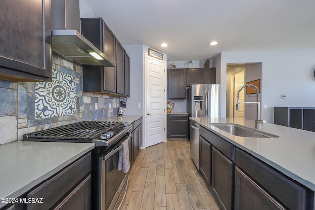 kitchen featuring stainless steel appliances, light wood-type flooring, wall chimney range hood, backsplash, and sink