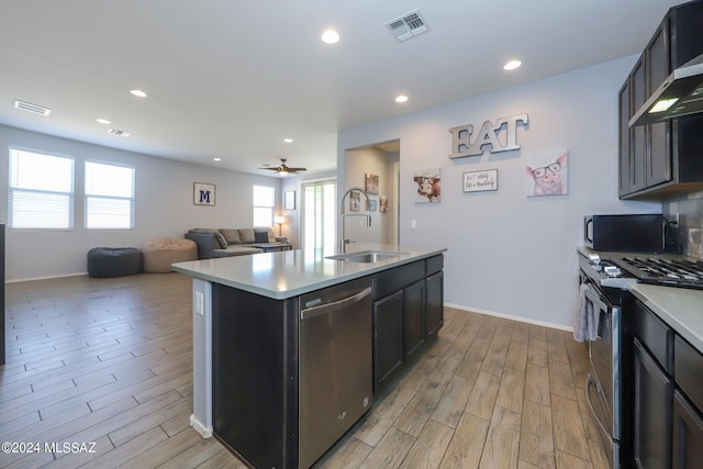 kitchen with sink, a kitchen island with sink, ceiling fan, light wood-type flooring, and appliances with stainless steel finishes