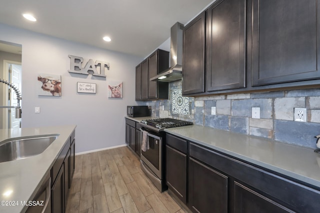 kitchen featuring decorative backsplash, light hardwood / wood-style flooring, sink, wall chimney range hood, and appliances with stainless steel finishes