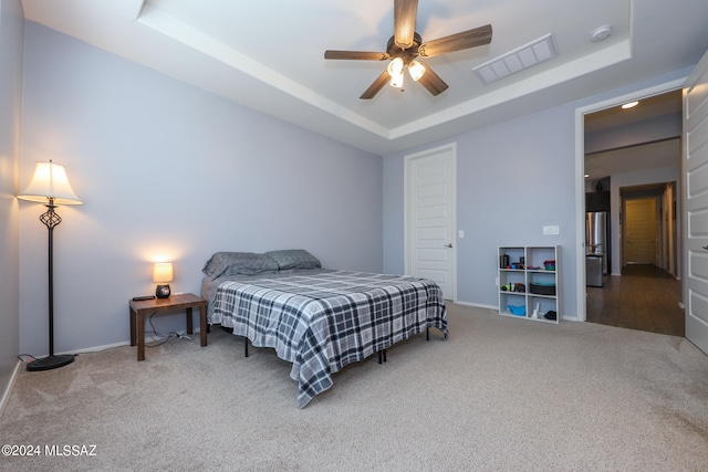 carpeted bedroom with ceiling fan, a raised ceiling, and stainless steel fridge