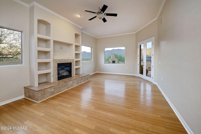 unfurnished living room with ornamental molding, ceiling fan, a tile fireplace, built in features, and light hardwood / wood-style floors