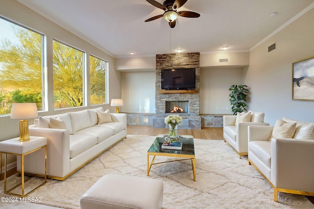 living room featuring a stone fireplace, ceiling fan, light hardwood / wood-style flooring, and ornamental molding