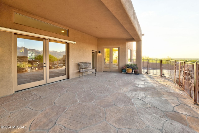 patio terrace at dusk with a mountain view, a balcony, and french doors